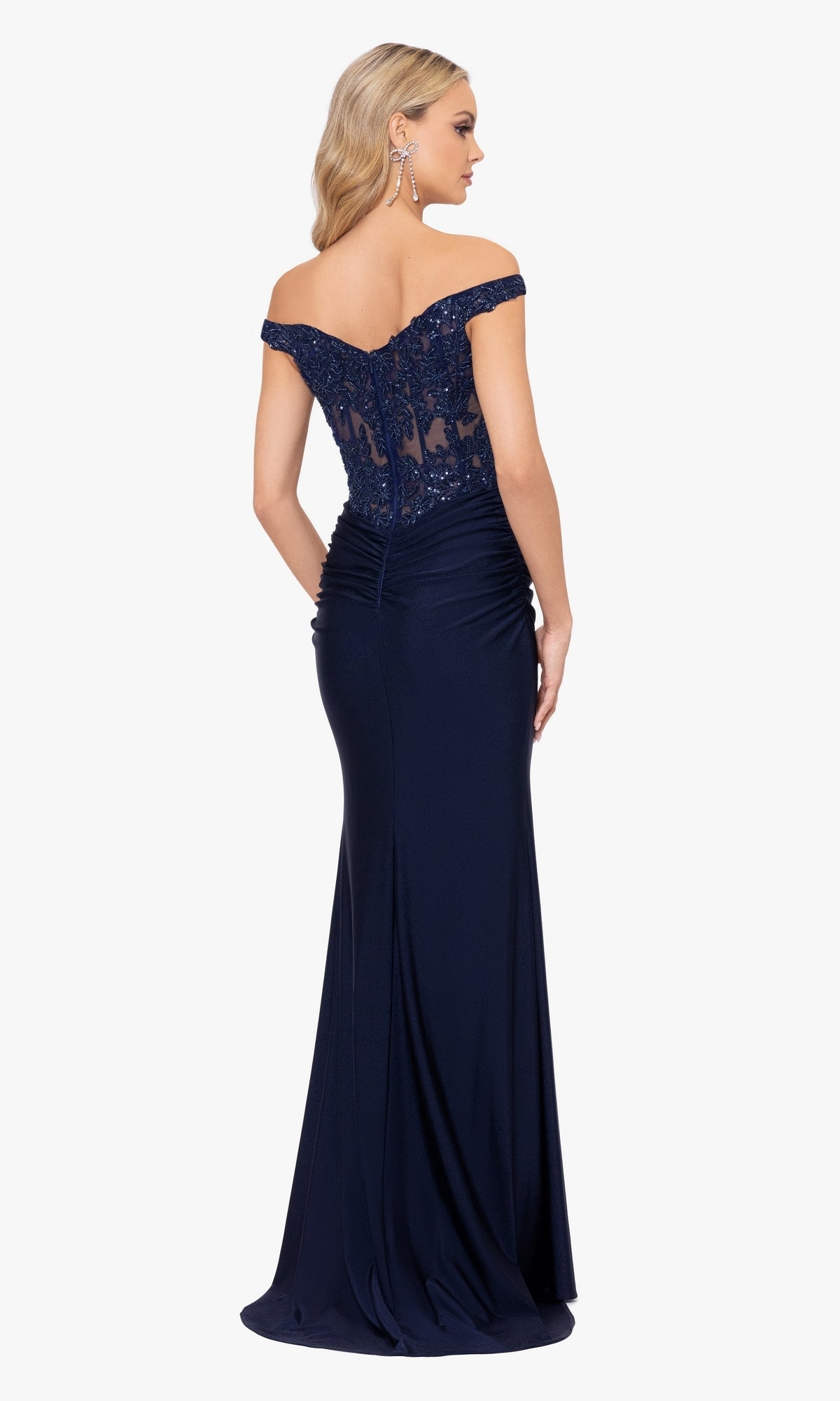 Woman wearing the Off-the-Shoulder Long Navy Prom Dress A26276, featuring lace detailing and a fitted skirt, poses with her back to the camera for an elegant evening look.